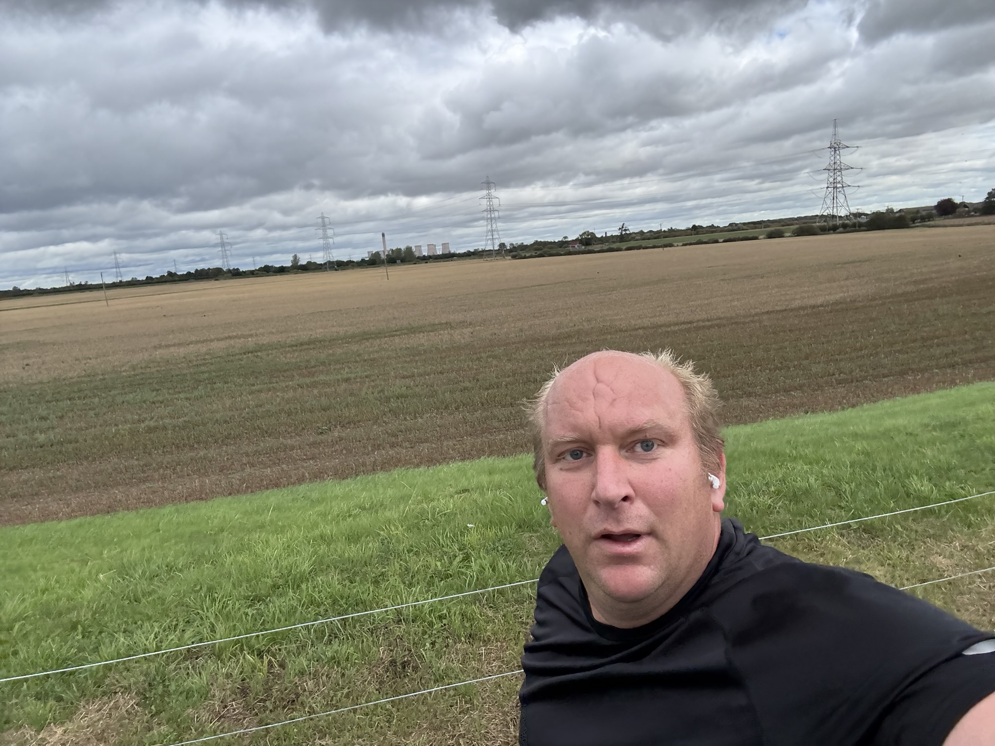 Chris taking a selfie beside open fields during a run, beneath a cloudy sky.