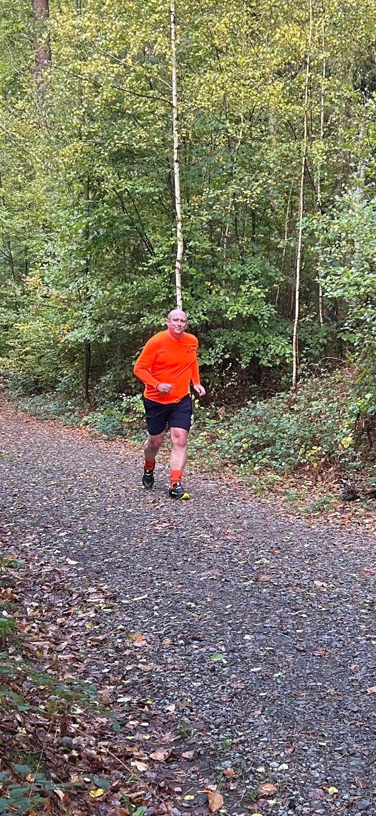 Chris running along a woodland path in his bright orange JOG ON top.
