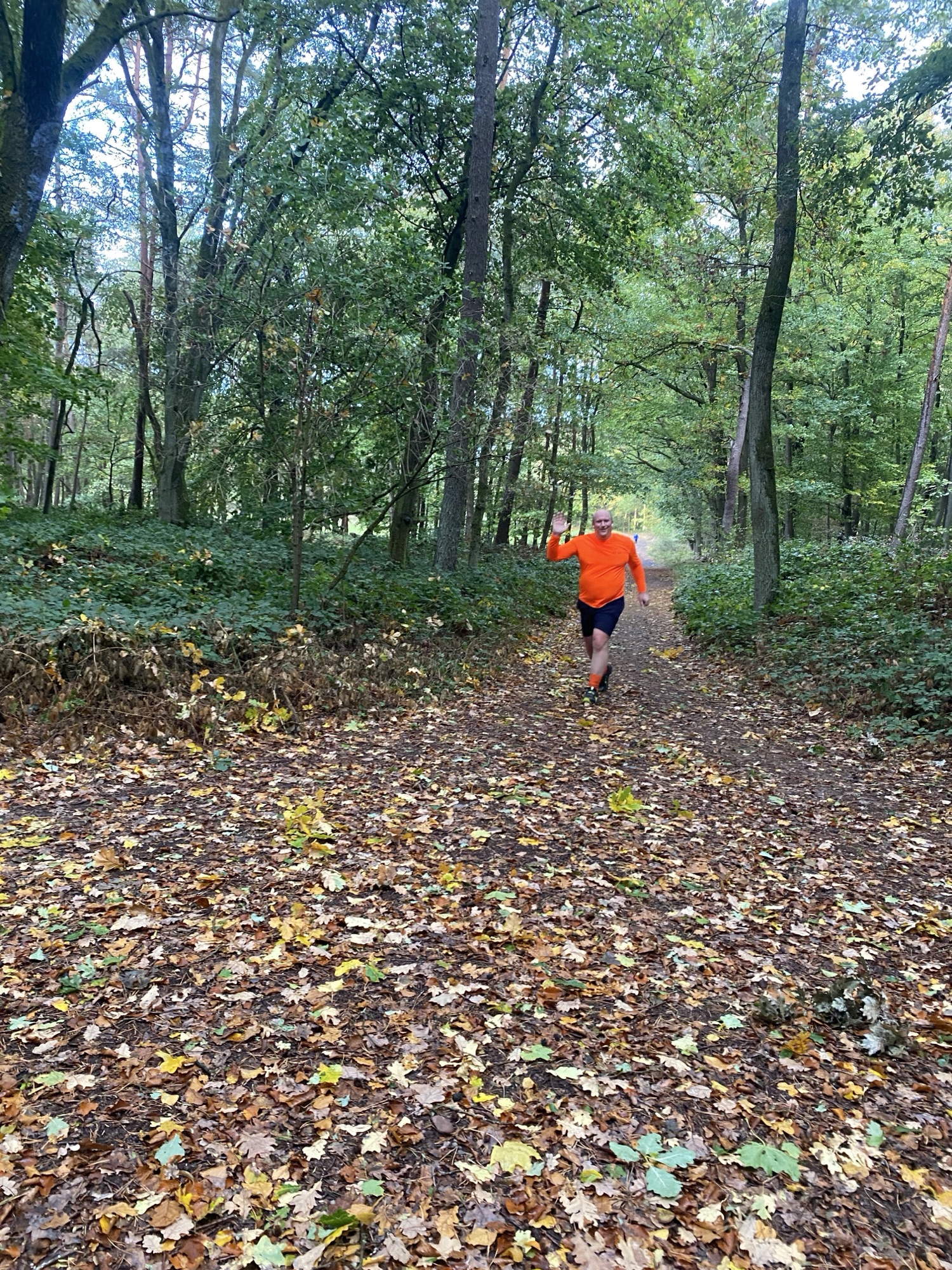 Chris waving while running through autumn woodland in his orange JOG ON top.